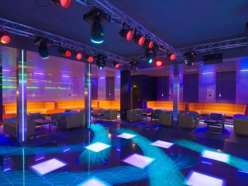 Lounge colorata in discoteca con divani in pelle ed effetti luce vibranti sul pavimento.
