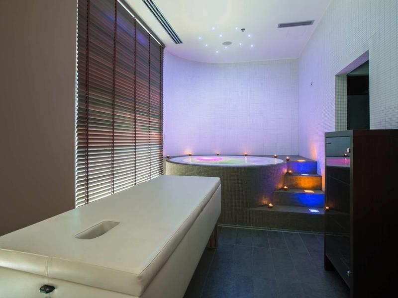 Stanza spa con lettino da massaggio e grande vasca idromassaggio rotonda con illuminazione d'atmosfera.