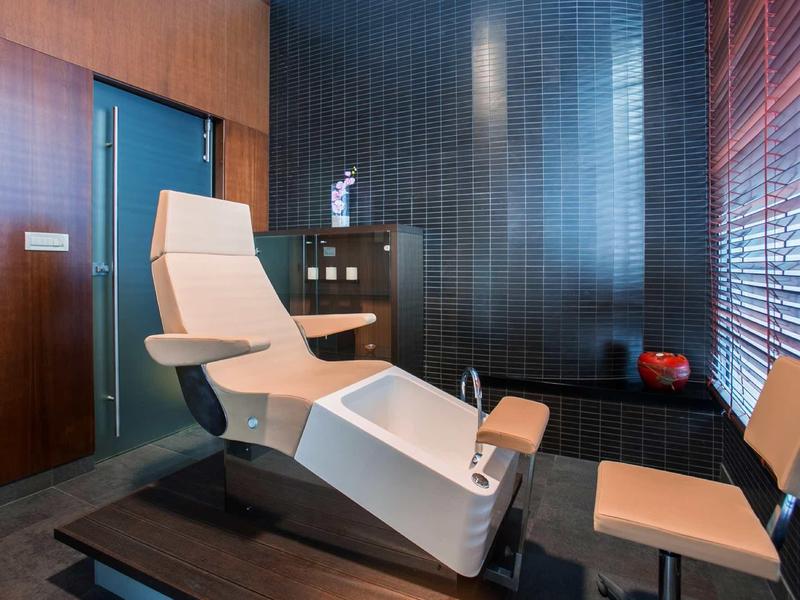 Camera spa moderna con poltrona reclinabile, luce calda e pareti in legno.