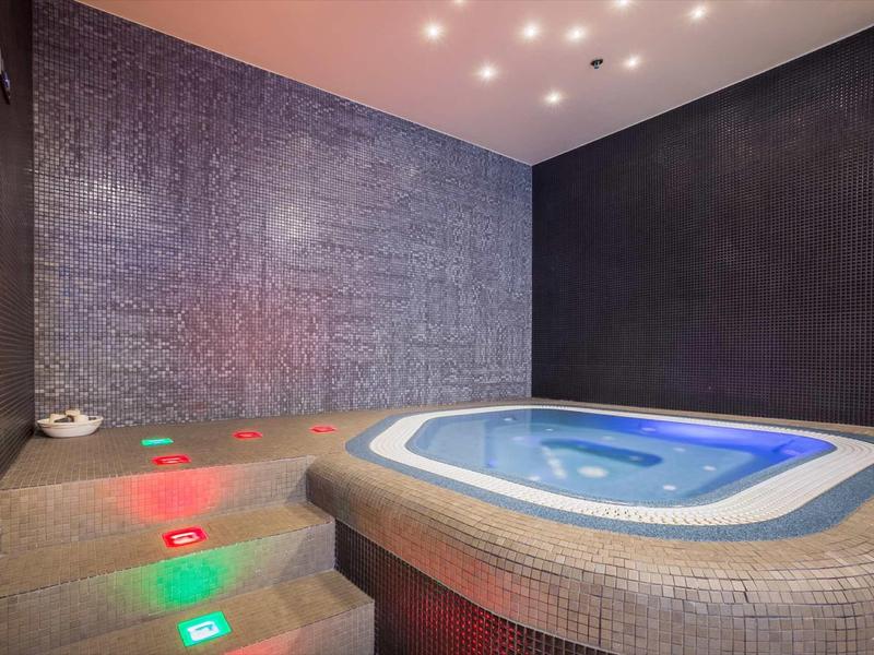 Idromassaggio interno con luci colorate sui gradini in una stanza spa moderna.