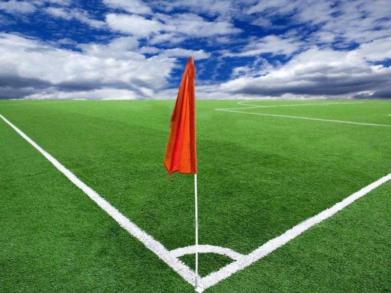 Angolo di campo da calcio verde con una bandiera rossa sotto un cielo blu con nuvole