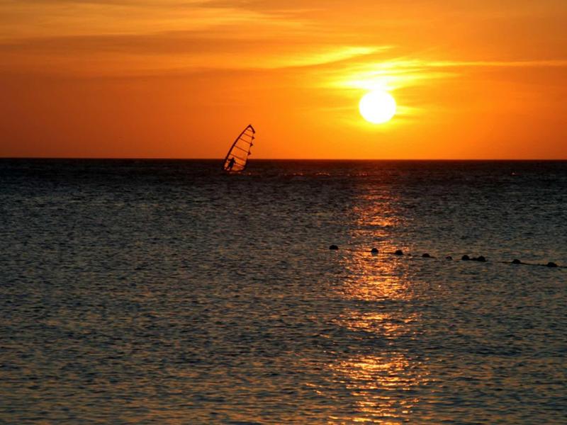Tramonto sul mare calmo con un windsurfista in silhouette contro il cielo arancione
