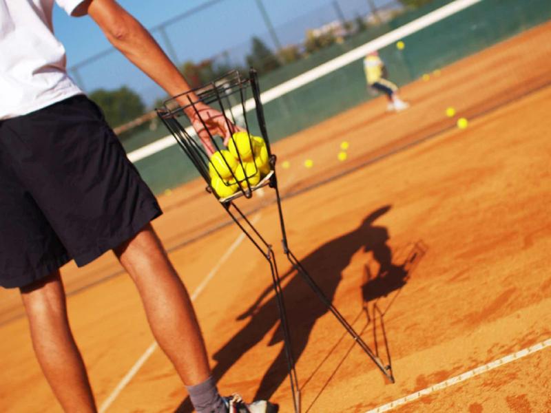 Persona che raccoglie palline da tennis su un campo in terra battuta con un raccoglitore.