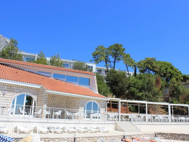 Building with red roof and white walls surrounded by green trees under a clear blue sky.