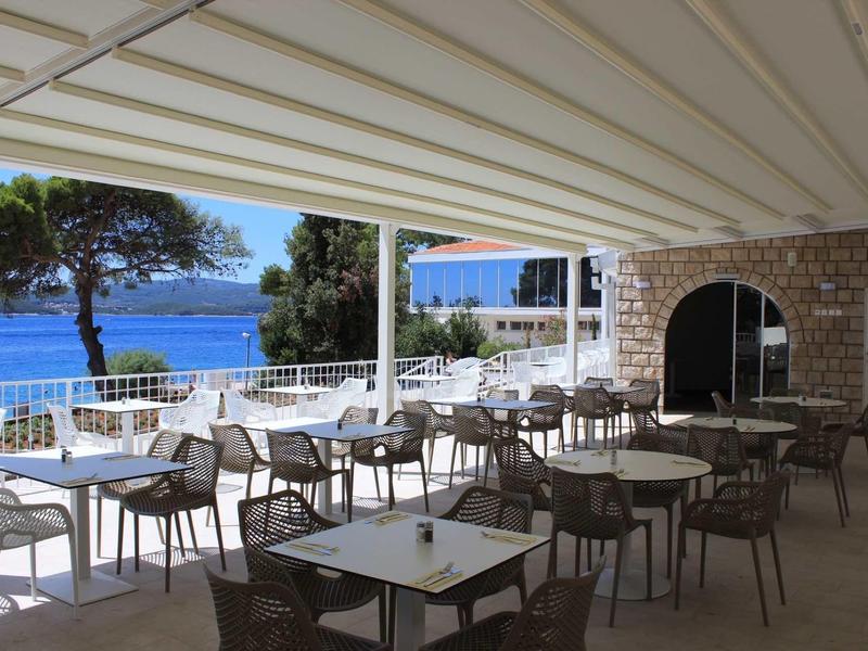 Covered terrace with seating and a view of the sea and trees.