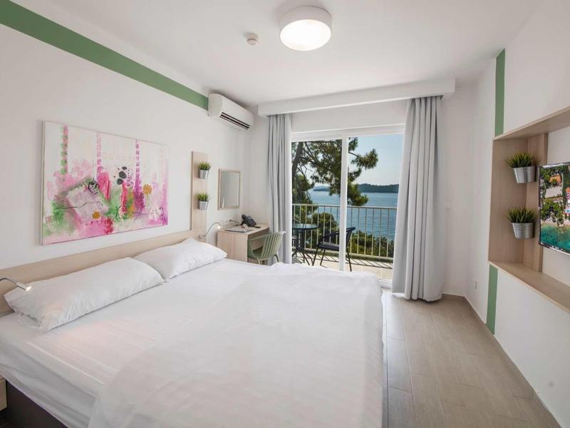 Bright hotel room with double bed, sea view, and balcony seating area.