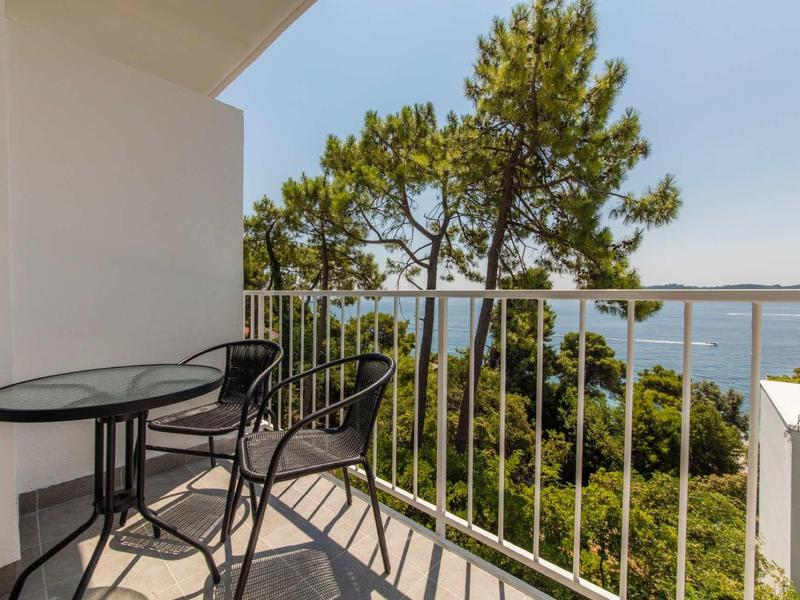 Balcony with black table and chairs overlooking trees and sea in the background.