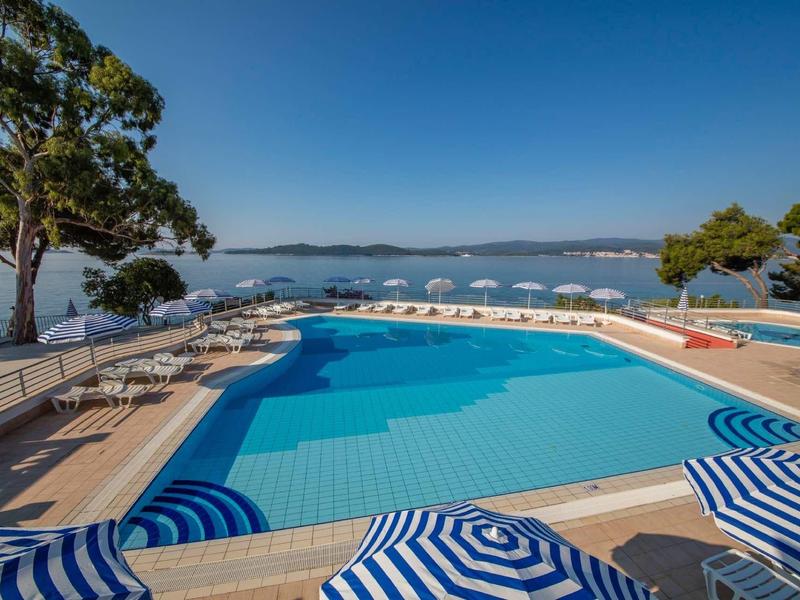 Large pool with blue loungers and sea view under clear sky.