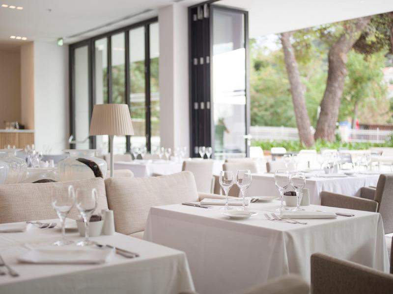 Ristorante luminoso con grandi finestre e tavoli apparecchiati in bianco e beige.