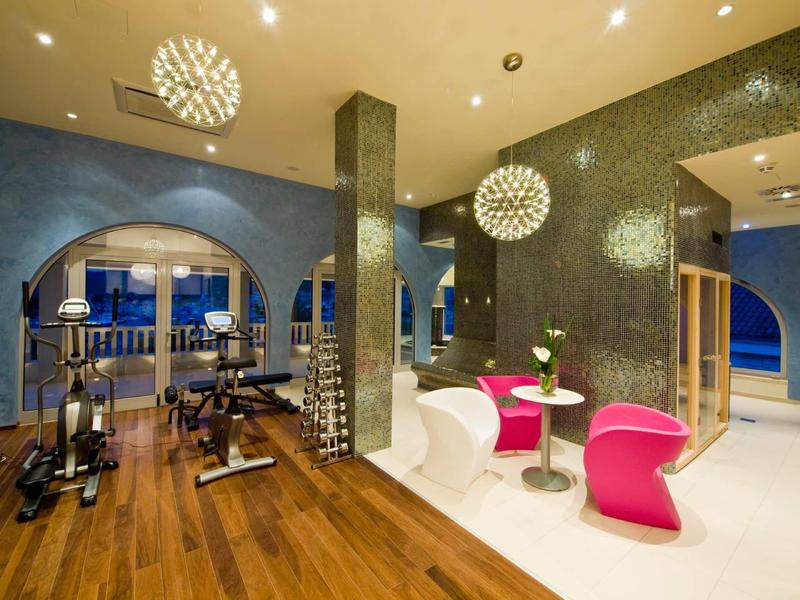 Area fitness moderna con sedie rosa e vista sul mare al crepuscolo.