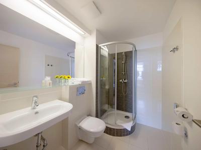 Světlá, moderní koupelna s kulatým sprchovým koutem, umyvadlem, toaletou a velkým zrcadlem.