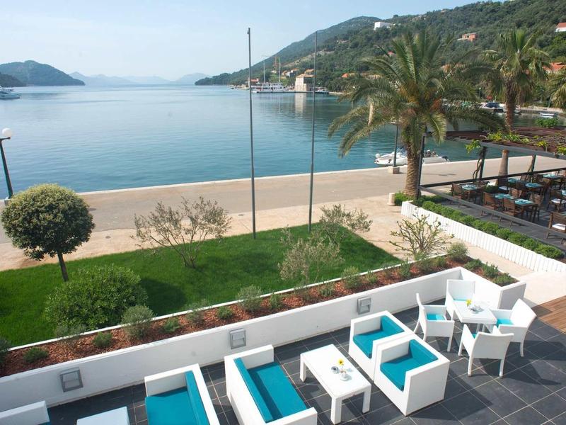 Taras z białymi i niebieskimi miejscami do siedzenia z widokiem na plażę i góry w tle.