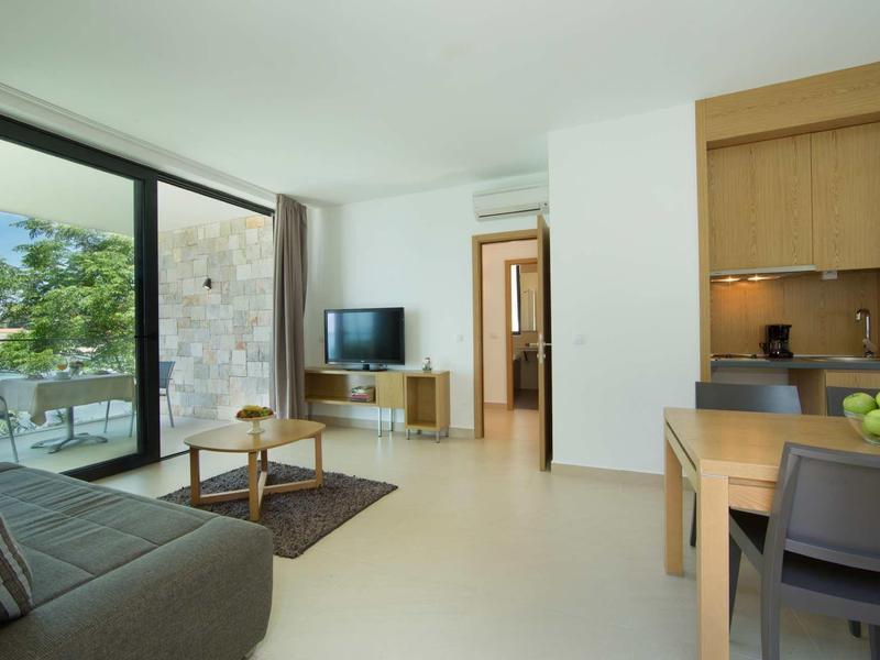 Moderne hotelkamer met zithoek, tv en groot raam met uitzicht op terras en zee.