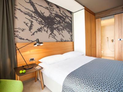 Camera d'hotel moderna con letto matrimoniale, arte astratta sulla parete e zona salotto verde.