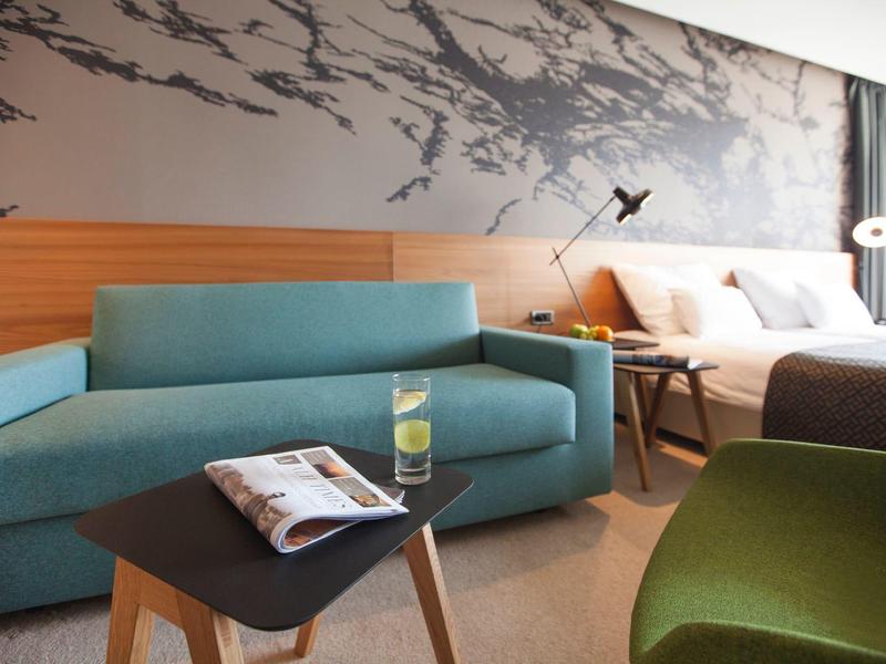 Habitación de hotel moderna con sofá azul, mesa con bebida y revista.