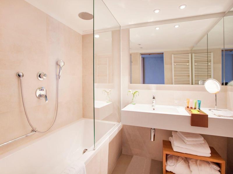 Baño luminoso con bañera, mampara de vidrio y espejo grande sobre el lavabo.