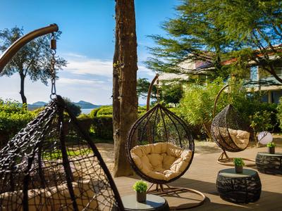 Terrasse mit modernen Hängesesseln, Sitzkissen und Bäumen an einem sonnigen Tag