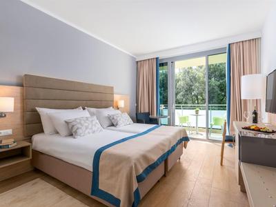 Modernes Schlafzimmer mit Doppelbett, großen Fenstern, hellen Vorhängen und Holzfußboden.