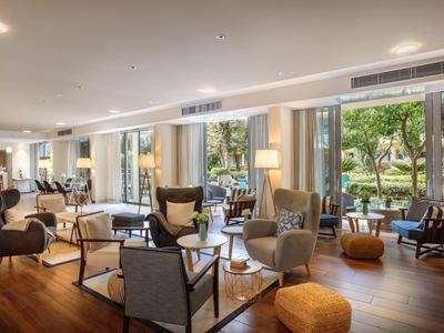 Heller, moderner Wohnraum mit großen Fenstern, bequemen Sesseln und Naturblick im Hintergrund.