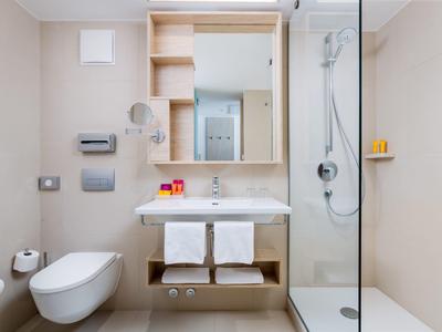 Modernes Badezimmer mit fliegender Toilette, Waschbecken, Spiegel und Duschkabine rechts.