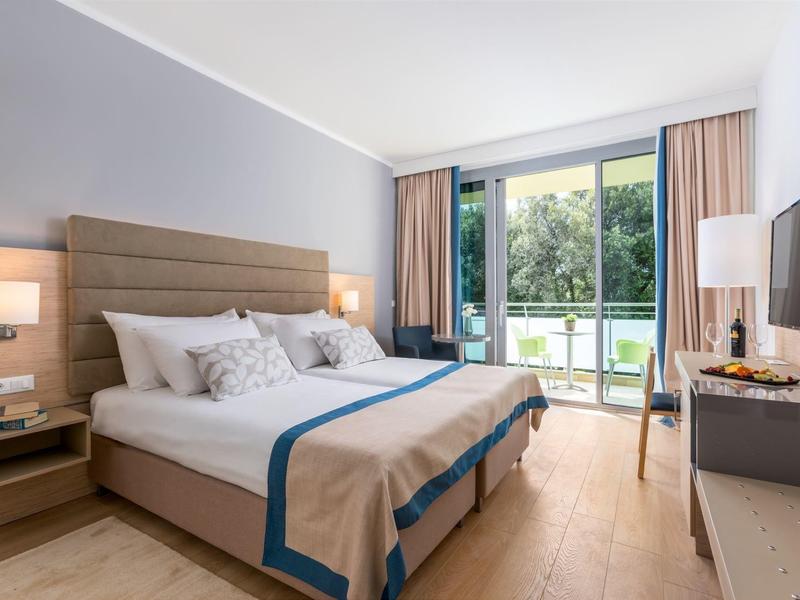 Modernes Schlafzimmer mit Doppelbett, großen Fenstern, hellen Vorhängen und Holzfußboden.