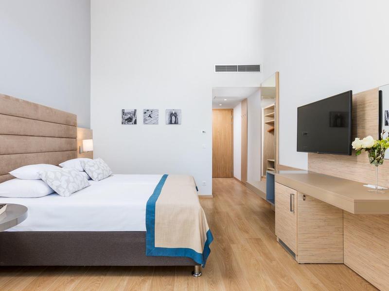 Modernes Schlafzimmer mit großem Bett, hellem Holzboden, Schreibtisch und Wandfernseher.