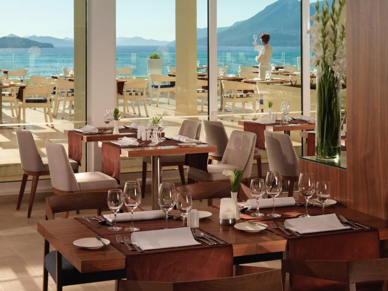 Elegantní restaurace s dřevěnými stoly a výhledem na moře a hory.