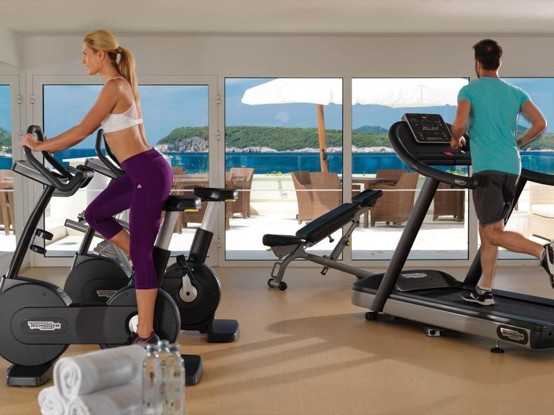 Dva lidé cvičí v jasné posilovně s velkými okny s výhledem na moře.