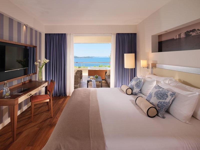 Pohodlný hotelový pokoj s velkou postelí, psacím stolem a balkonem s výhledem na moře.