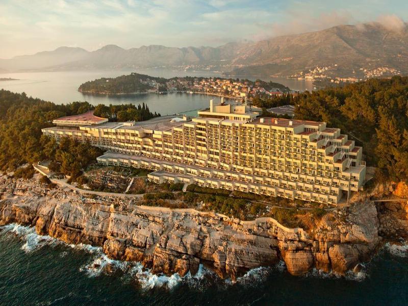 Hotel on a rocky peninsula overlooking the sea and wooded hills at sunset.