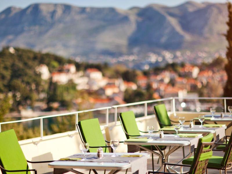 Hotel terrace area with green chairs and mountain view in the background.
