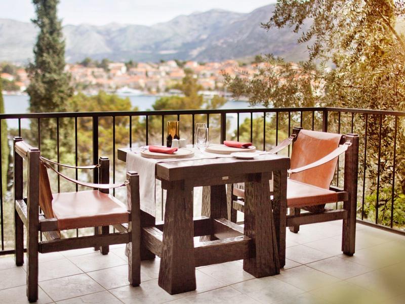 Two chairs and a table on a balcony overlooking mountains and a town.