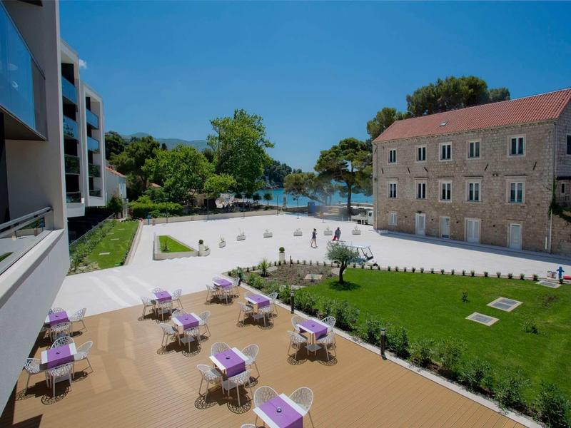 Moderní hotelová zóna s terasou, zahradou a historickou kamennou budovou u vody.