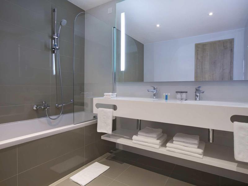 Moderní koupelna s vanou, velkým zrcadlem a umyvadlem s ručníky.