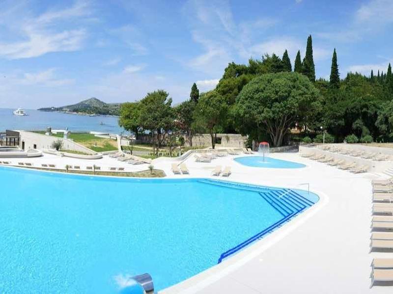 Velký bazén s modrou vodní plochou a lehátky na slunném pobřežním letovisku.