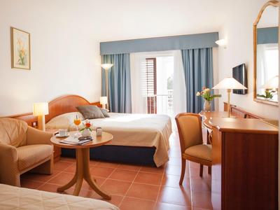 Jasny pokój hotelowy z dwoma łóżkami, miejscem do siedzenia i biurkiem z krzesłem oraz lustrem.