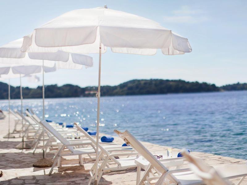 Plaża z białymi leżakami i parasolami wzdłuż kamiennej ścieżki nad morzem.