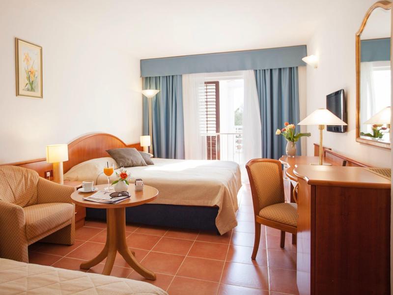 Jasny pokój hotelowy z łóżkiem podwójnym, sofą, stołem i biurkiem z lustrem.