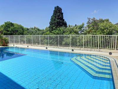 Klares blaues Schwimmbad mit weißen Stufen und Geländer, umgeben von Bäumen und blauem Himmel.