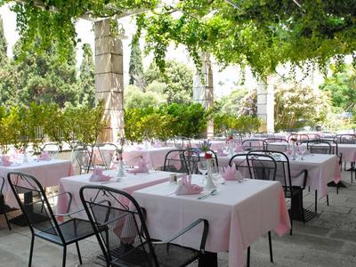 Überdachter Außenbereich eines Restaurants mit weißen Tischdecken und Stühlen unter grünen Pflanzen.