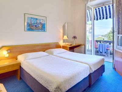 Hotelzimmer mit zwei Einzelbetten, Schreibtisch, Balkon mit Aussicht und blauem Teppichboden.