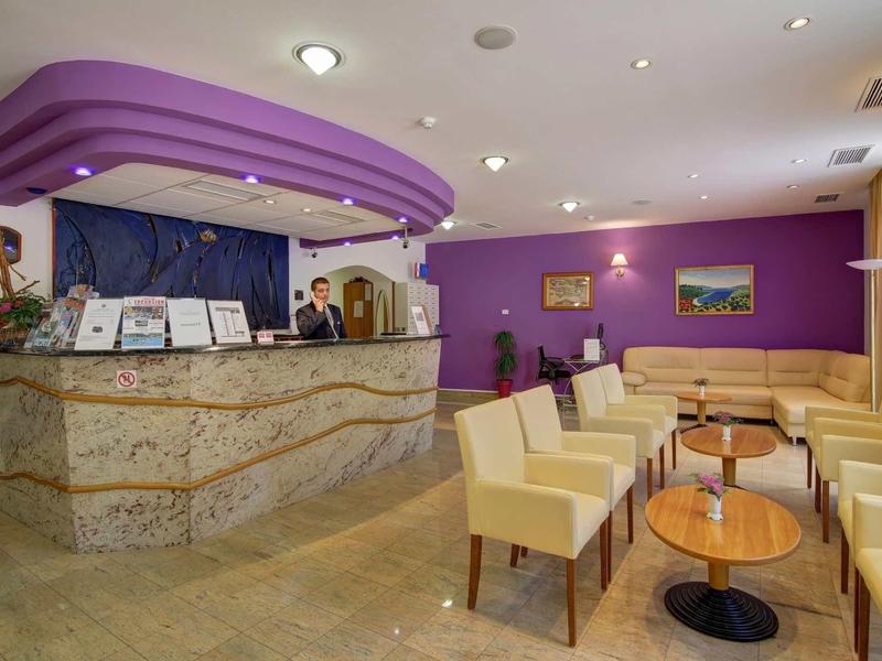 Moderne hotel lobby met paarse receptiebalie, beige stoelen en tafels.