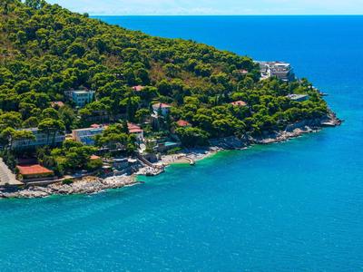 Littoral avec eau bleue claire, colline boisée et maisons au bord de la rive.