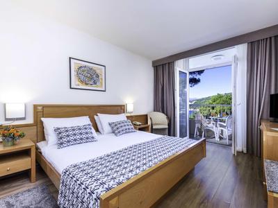 Chambre d'hôtel lumineuse avec lit double, meubles en bois et balcon offrant une vue sur des arbres verts.