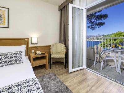 Chambre d'hôtel avec balcon, vue sur la mer, lit, fauteuil et table avec chaises.