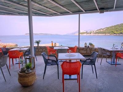 Terrasse couverte avec tables et chaises offrant une vue sur la mer et les collines en arrière-plan.