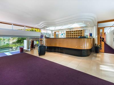 Réception d'hôtel moderne avec comptoir en bois, tapis violet et grandes fenêtres donnant sur l'extérieur.