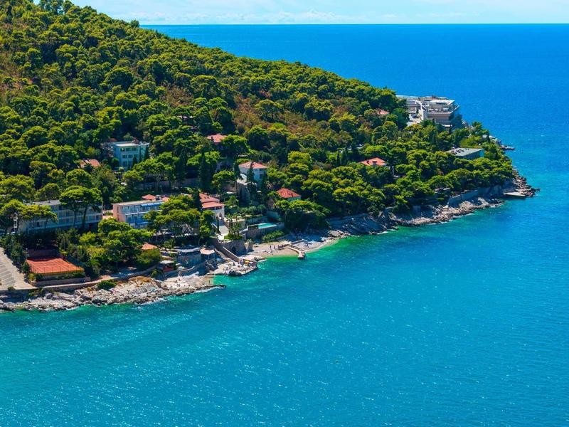 Littoral avec eau bleue claire, colline boisée et maisons au bord de la rive.
