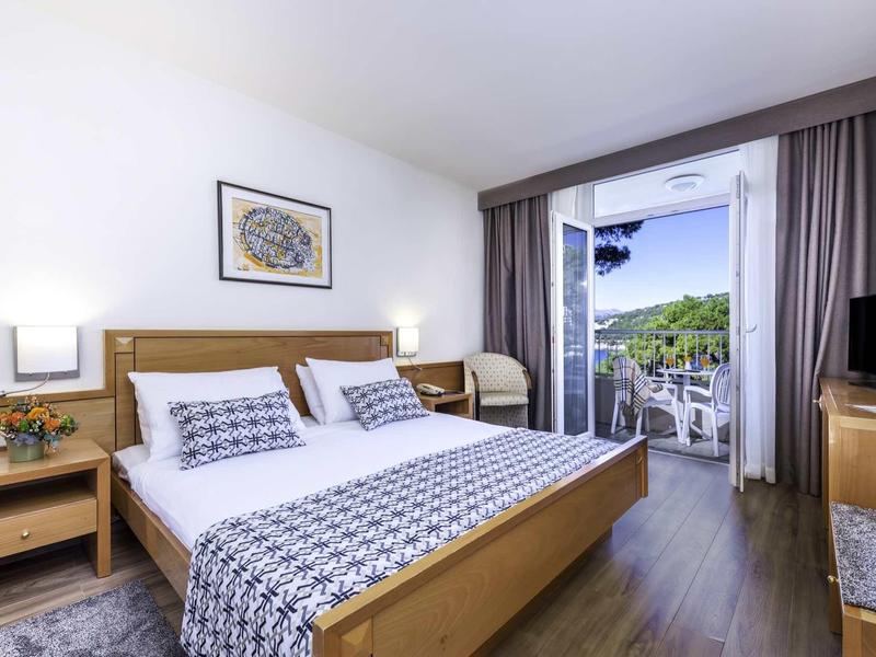 Chambre d'hôtel lumineuse avec lit double, meubles en bois et balcon offrant une vue sur des arbres verts.