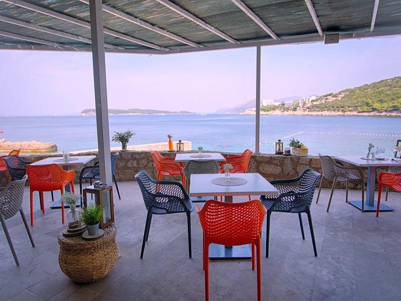 Terrasse de restaurant ouverte avec des chaises colorées et vue sur la mer sous un ciel clair.